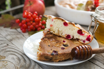 a piece of apple pie, next to it is a sprig of viburnum, honey and a honey spoon. autumn atmosphere. wooden background