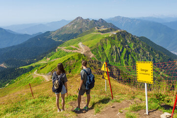 Tourists a guy and a girl with backpacks are standing on the slope of alpine meadows enjoying the...