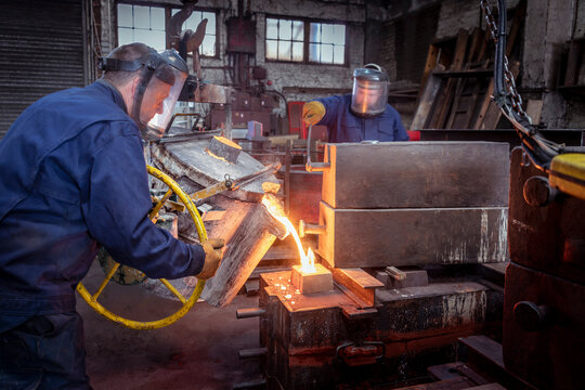 Worker pouring molten metal into mold in iron foundry