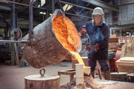Worker pouring molten brass into large mold in brass foundry