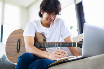 Young composer man composing song with guitar and laptop at home. Selective focus of musician's hand