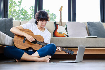 Young man playing guitar and learning a new song with laptop, guitarist musician lifestyle