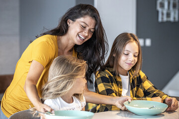 Teenage and little girl waiting for breakfast Mom in background carrying plates with food