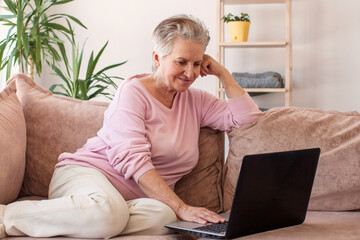 Older smiling 60s woman sitting at home on sofa