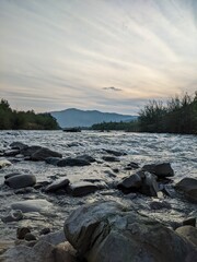 Beautiful cloudy sky at sunset over the river. The high bank of the river is overgrown with grass.