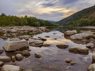 Beautiful cloudy sky at sunset over the river. The high bank of the river is overgrown with grass.