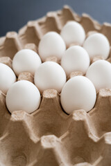 Natural chicken eggs in carton tray on blurred grey background.