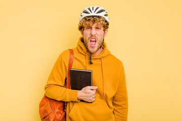 Young student man wearing a helmet bike isolated on yellow background screaming very angry and aggressive.