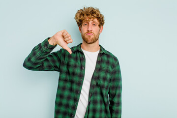 Young caucasian man isolated on blue background showing a dislike gesture, thumbs down....