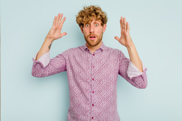 Young caucasian man isolated on blue background celebrating a victory or success, he is surprised and shocked.