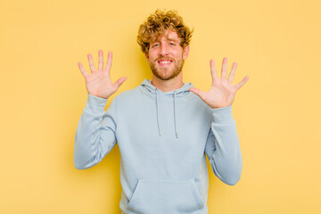 Young caucasian man isolated on yellow background showing number ten with hands.