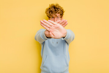 Young caucasian man isolated on yellow background doing a denial gesture