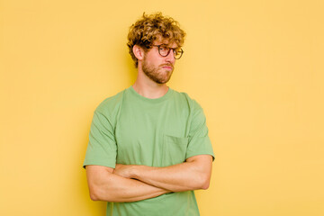 Young caucasian man isolated on yellow background suspicious, uncertain, examining you. - obrazy, fototapety, plakaty