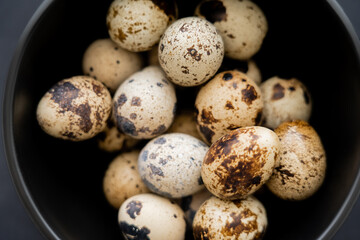 Close up view of fresh quail eggs in bowl on black background.