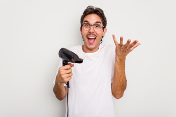 Young hispanic man holding a hairdryer isolated on white background receiving a pleasant surprise, excited and raising hands.