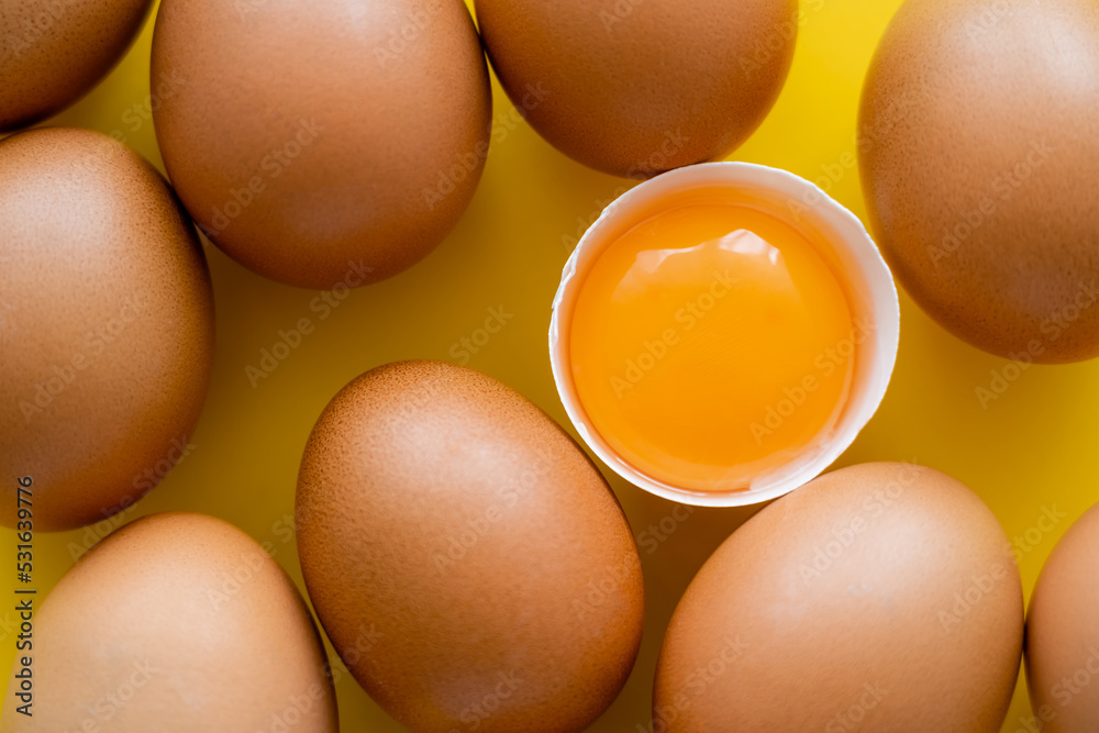 Poster Close up view of fresh yolk in shell near eggs on yellow background.