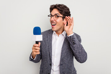 Naklejka premium Young hispanic TV presenter man isolated on white background trying to listening a gossip.