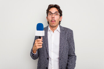 Naklejka premium Young hispanic TV presenter man isolated on white background shrugs shoulders and open eyes confused.