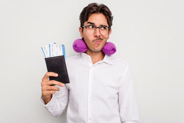 Young hispanic man with inflatable travel pillow holding passport isolated on white background confused, feels doubtful and unsure.