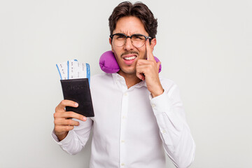 Young hispanic man with inflatable travel pillow holding passport isolated on white background showing a disappointment gesture with forefinger.