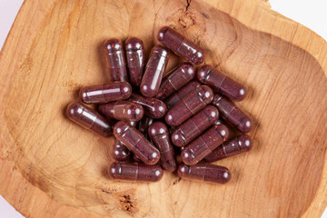 Health capsules with bilberry extract in a rustic wooden bowl