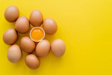 Top view of yolk in shell near eggs on yellow background.