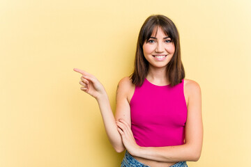 Young caucasian woman isolated on yellow background smiling cheerfully pointing with forefinger away.