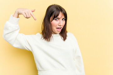 Young caucasian woman isolated on yellow background person pointing by hand to a shirt copy space, proud and confident