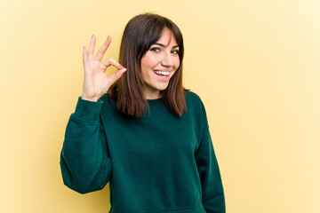 Young caucasian woman isolated on yellow background cheerful and confident showing ok gesture.