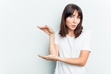Young caucasian woman isolated on white background shocked and amazed holding a copy space between hands.