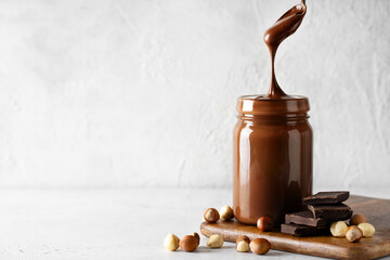 Chocolate paste in jar with nuts on cut wooden board