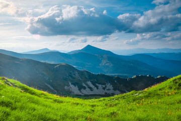 Fototapeta premium Idyllic spring landscape in the Alps with fresh green meadow and mountain range tops in the background. Morning alpine highlands in sunny day. Beautiful nature landscape. Popular tourist destination