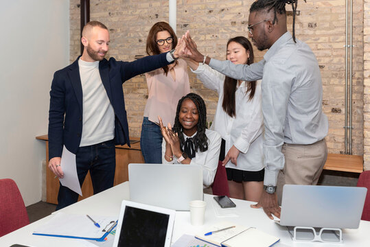 Multi-ethnic Employees Sales Team Giving High Five Together Celebrating Corporate Success And Teamwork Result, Diverse Group Of Office People Joining Hands Excited By Common Victory Achievement