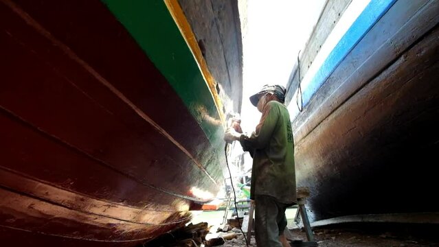 A craftsman smooths the surface of a ship's hull with a grinder