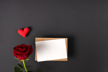 A red rose and a mock-up of a kraft envelope with a blank sheet on a black background. Banner for Valentine's Day. Postcard for February 14. Love. Minimalism.