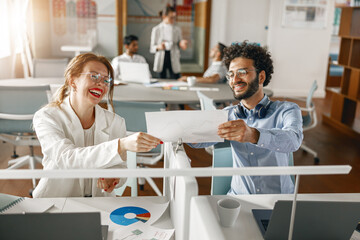 Two young diverse coworkers analyzing sales report while working together in the office