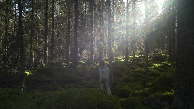 Rear view of young girl wonder lost in mossy deep forest, light shining through