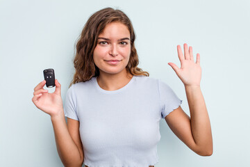 Fototapeta premium Young caucasian woman holding car keys isolated on blue background smiling cheerful showing number five with fingers.