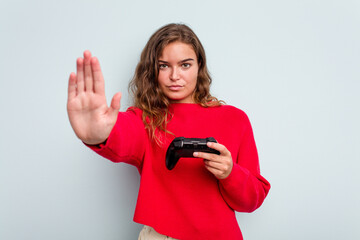 Young caucasian gamer woman holding a game controller isolated on blue background standing with outstretched hand showing stop sign, preventing you. © Asier
