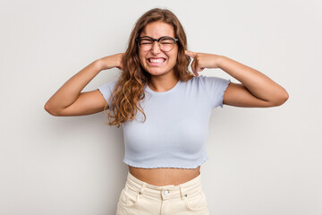 Young caucasian woman isolated on blue background covering ears with fingers, stressed and desperate by a loudly ambient.