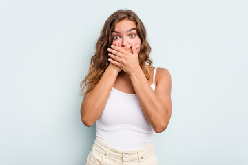 Young caucasian woman isolated on blue background covering mouth with hands looking worried.