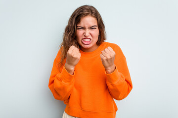 Young caucasian woman isolated on blue background showing fist to camera, aggressive facial expression.