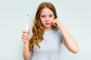 Young caucasian woman holding electric toothbrush isolated on blue background with fingers on lips keeping a secret.