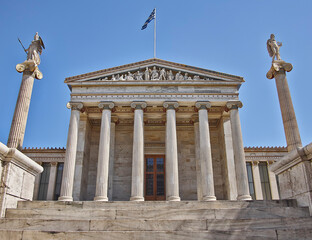 Fototapeta na wymiar The national university of Athens neoclassical front, Greece. Athena and Apollo ancient gods marble statues are standing on corinthian rythm columns, under the clear blue sky.