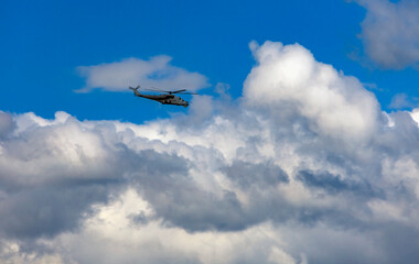 Russian combat helicopter is flying against the background of clouds in the summer sky.