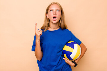 Little caucasian girl playing volleyball isolated on beige background pointing upside with opened...