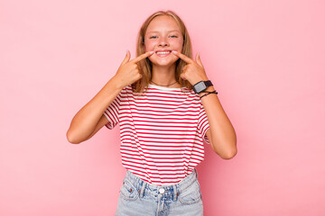 Caucasian teen girl isolated on pink background smiles, pointing fingers at mouth.