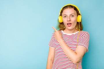 Young caucasian woman wearing headphones isolated on blue background pointing to the side