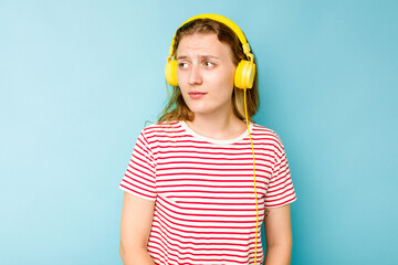 Young caucasian woman wearing headphones isolated on blue background confused, feels doubtful and unsure.