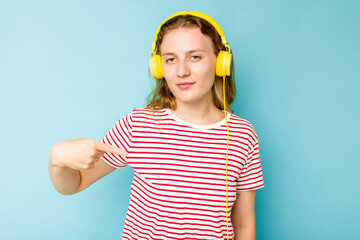 Young caucasian woman wearing headphones isolated on blue background person pointing by hand to a shirt copy space, proud and confident